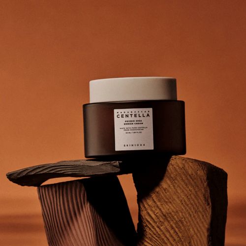 Skin1004 MADAGASCAR CENTELLA PROBIO-CICA ENRICH CREAM jar on wooden surface against orange background.